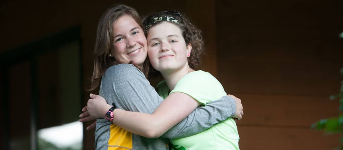 Camp counselor and camper hugging on deck.