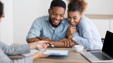 Happy African American couple looking at papers from woman assisting them 
