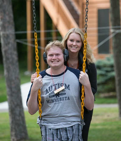 A camp counselor pushing her camper on a swing.