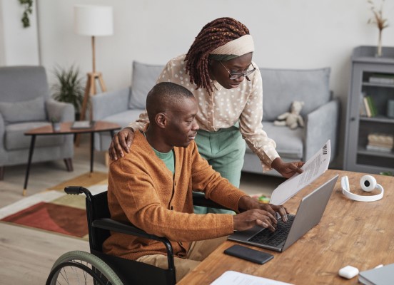 Man at a laptop using wheelchair and woman looking over document together 