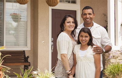 Family of three in front of house.