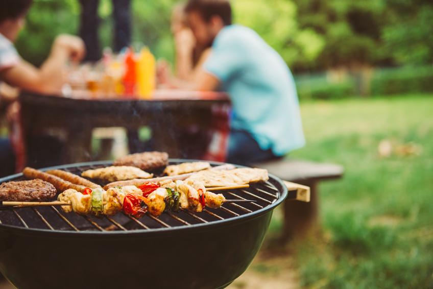 Family at a picnic table with meat cooking on a grill
