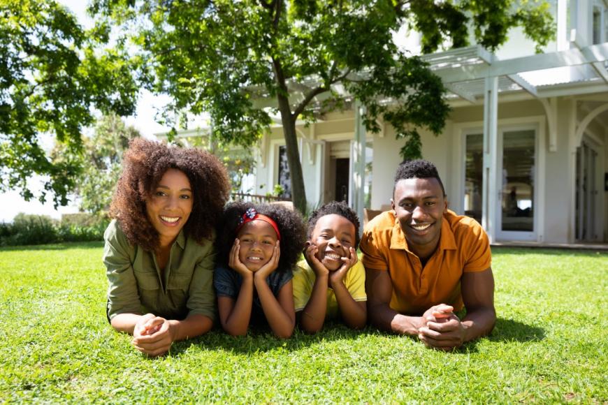 African American couple with two young children all lying on grass in front of house and smiling