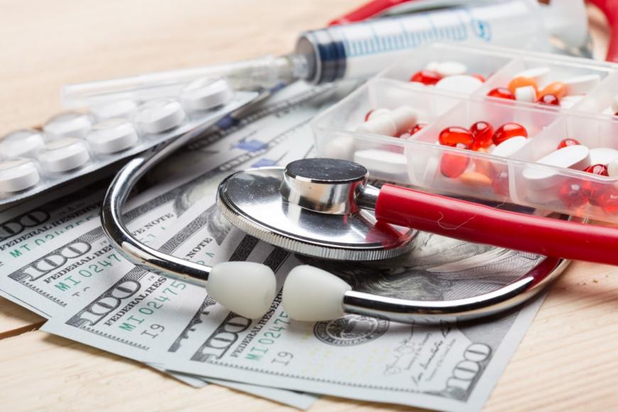Stethoscope, pills, and syringe lying on $100 bills
