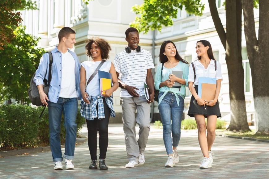 multiracial group of young adults walking togehter, carrying books, and enjoying each other's company