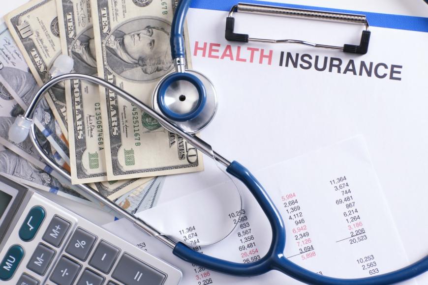 Stethoscope on top of ten-dollar bills and health insurance paperwork