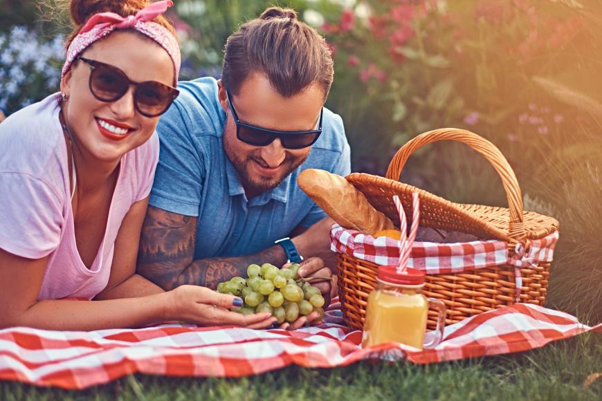 Woman and man lying on towel with bunch of grapes and a picnic basket next to them