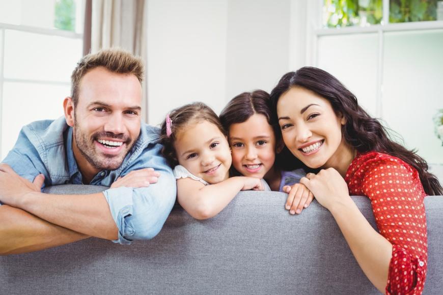 Man and woman with two young girls sitting on sofa and smiling at camera