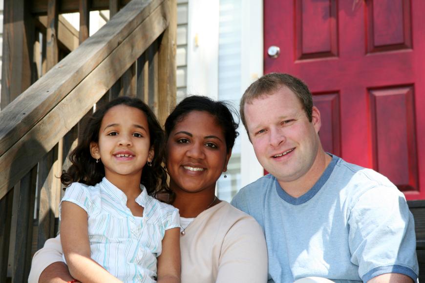 Multiracial family sitting on front steps of house
