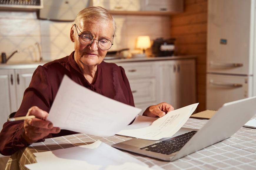 Older man sitting in front of his laptop, looking over paperwork