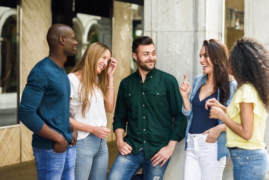 Multiracial group of adults standing outside next to a building, smiling and enjoying each other