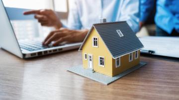couple working at laptop with miniature of a house next to the laptop