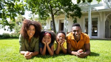 African American couple with two young children all lying on grass in front of house and smiling