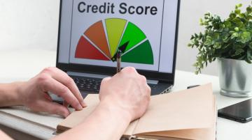 Person writing in notebook.  Graphic of Credit Score on laptop screen
