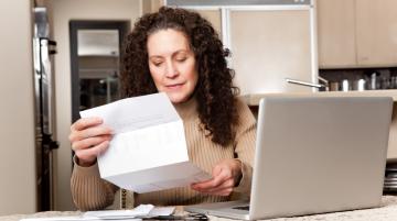 Middle-age woman looking at papers as whe sits in front of laptop