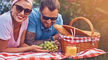 Woman and man lying on towel with bunch of grapes and a picnic basket next to them
