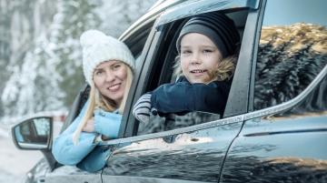 Young woman and child looking at camera from open car windows during winter months