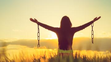 Woman facing sunset, arms extended widely to the sides.  Each arm has a broken chain