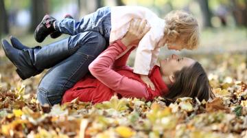 Woman playing with young child on the ground amongst fall leaves