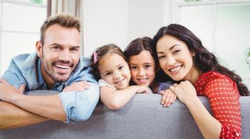Man and woman with two young girls sitting on sofa and smiling at camera