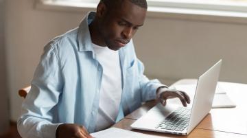 Man typing at a laptop while looking at paperwork