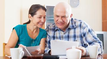 Older man and woman looking over paper smiling and holding coffee cups