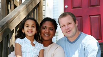 Multiracial family sitting on front steps of house