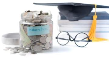 Jar filled with coins and labeled Education. To right of jar are a small stack of books with a graduation cap on top of them.