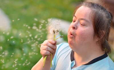 Girl with disability blowing a dandelion.