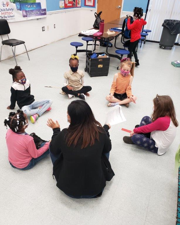 An adult and young children sit on the floor and participate in an activity together.