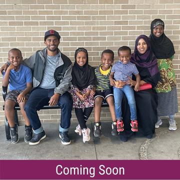Photo of Buni family, five children and two adults, sitting on a bench and smiling. Text saying "Coming Soon"